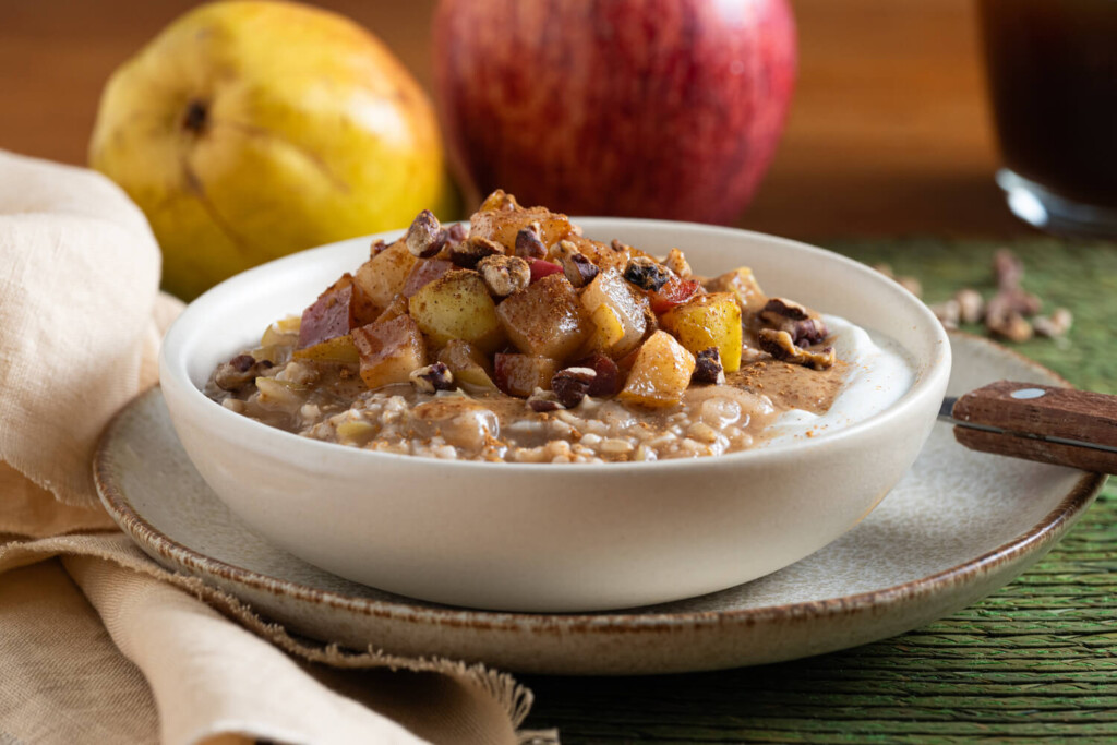 White bowl of steel cut oats garnished with apples and pears with apples in background
