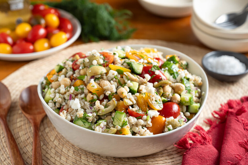 Image of a white bowl with a salad of barley, chickpeas, cucumbers, peppers, and tomatoes