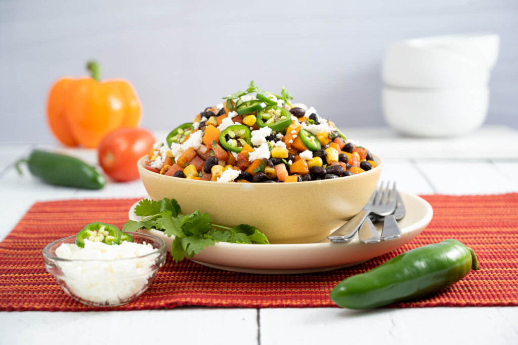 White bowl filled with a bean and corn salad finished with fresh jalapeno peppers, cilantro, and crumbled feta cheese for a colourful easy lunch
