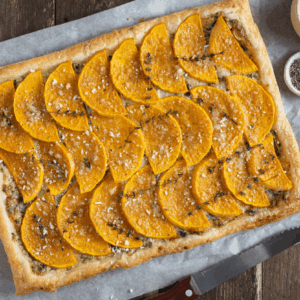 Overhead image of butternut squash tart with rows of butternut squash and fresh thyme sprigs