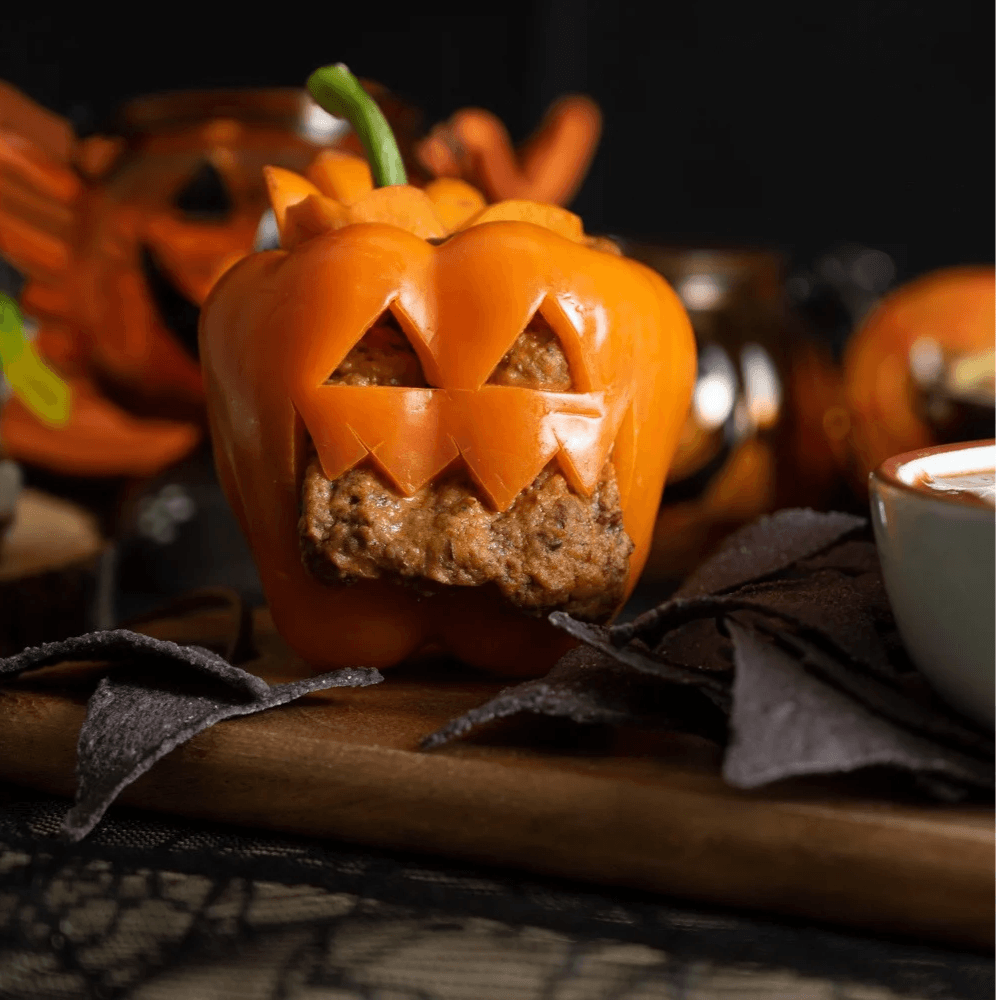 Orange bell pepper carved to look like a jack-o'-lantern filled with bean dip