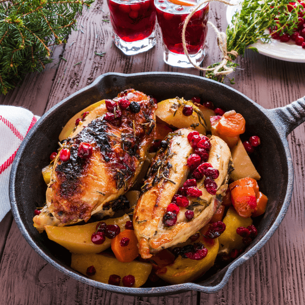 Baked chicken breast with carrots, cranberries and potatoes. Marinated with thyme, garlic and olive oil. Black cast-iron pan, wooden table.