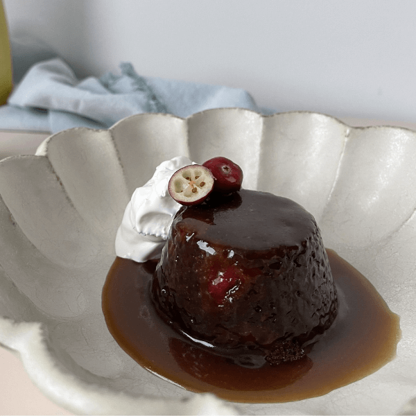 Scalloped white plate with a miniature sticky ginger cake with salted caramel sauce, whipped cream, and fresh cranberries 