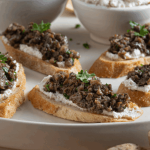 White plate with slices of crostini topped with mushroom duxelles mixture and fresh parsley