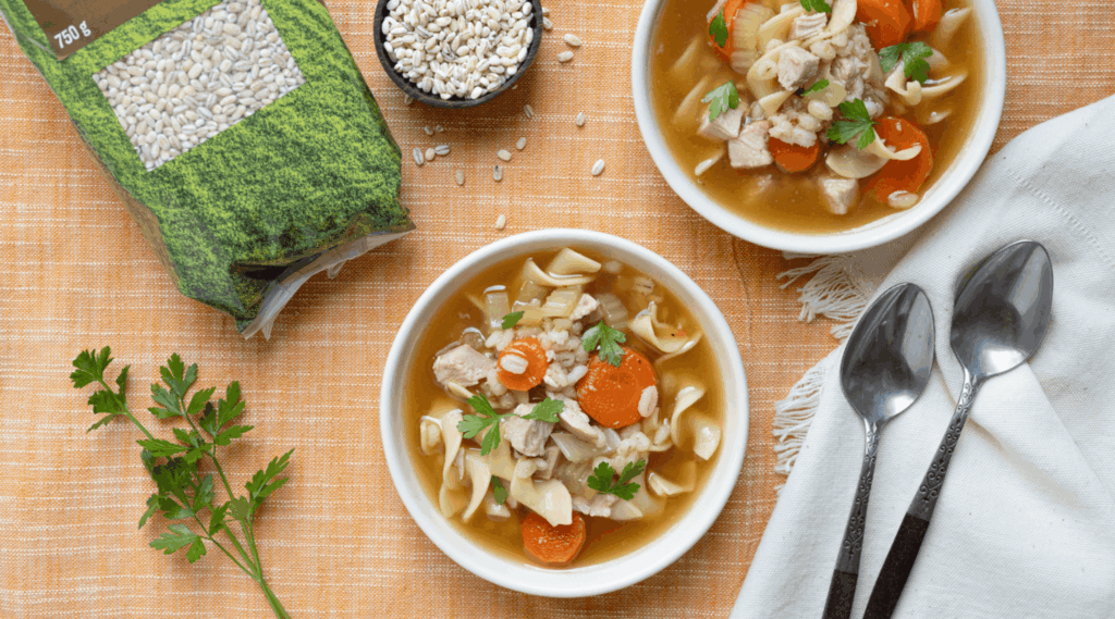 Overhead image of two bowl of turkey noodle soup with carrots, fresh parsley, and pearl barley