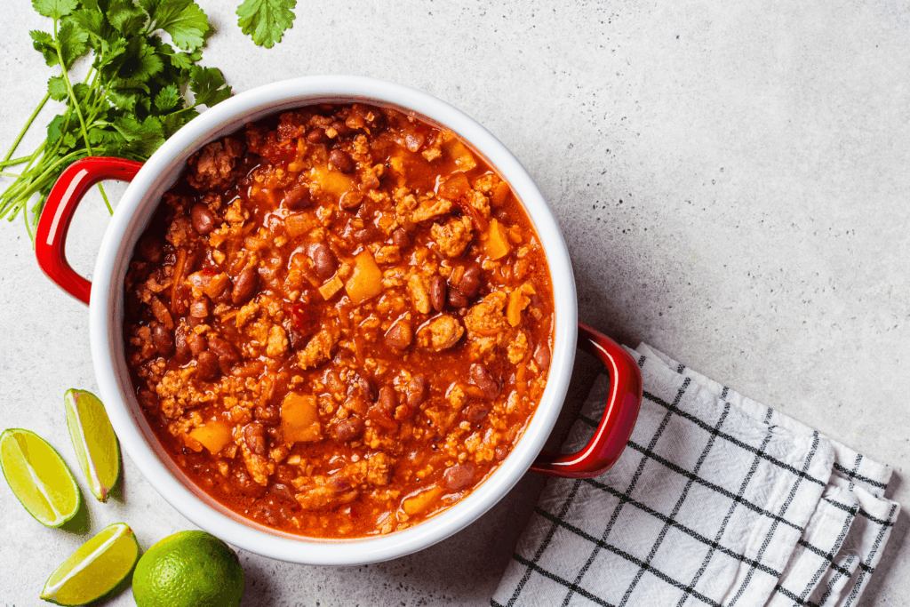 Vegan chili con carne with vegetables and beans in tomato sauce in red saucepan, top view