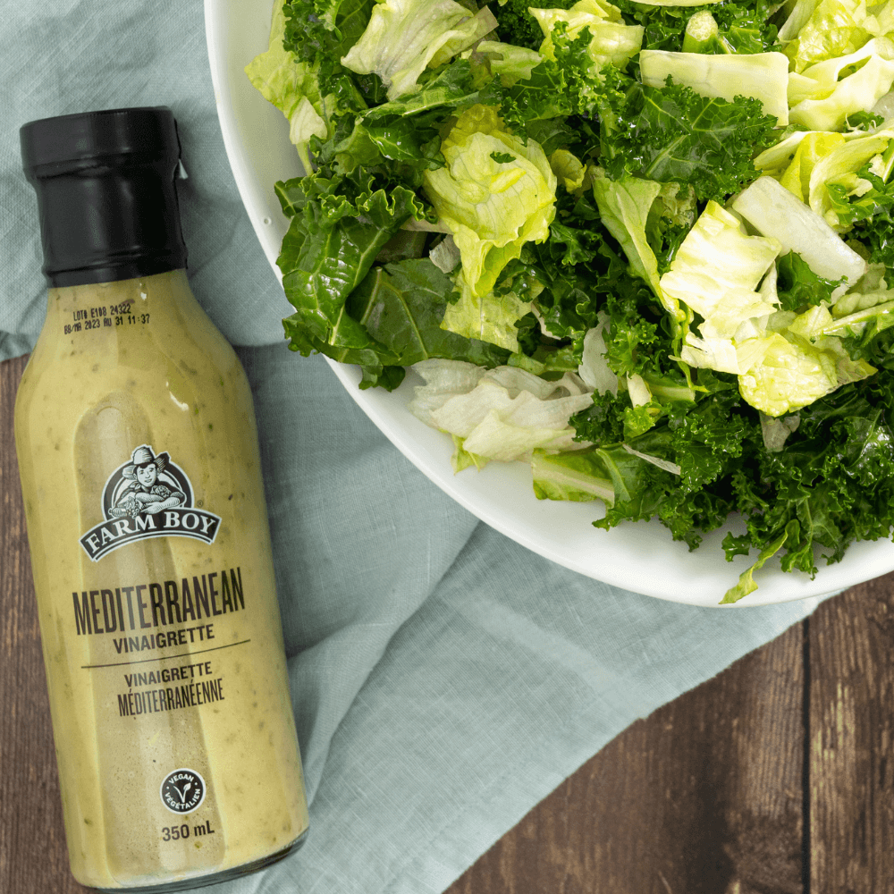 Overhead image of bowl of chopped lettuce greens beside bottle of Farm Boy Mediterranean Vinaigrette