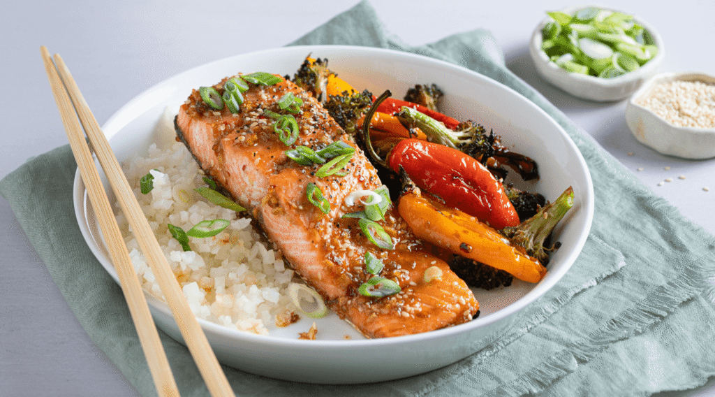 Bowl with fillet of teriyaki glazed salmon served with riced cauliflower, broccoli, and mini peppers