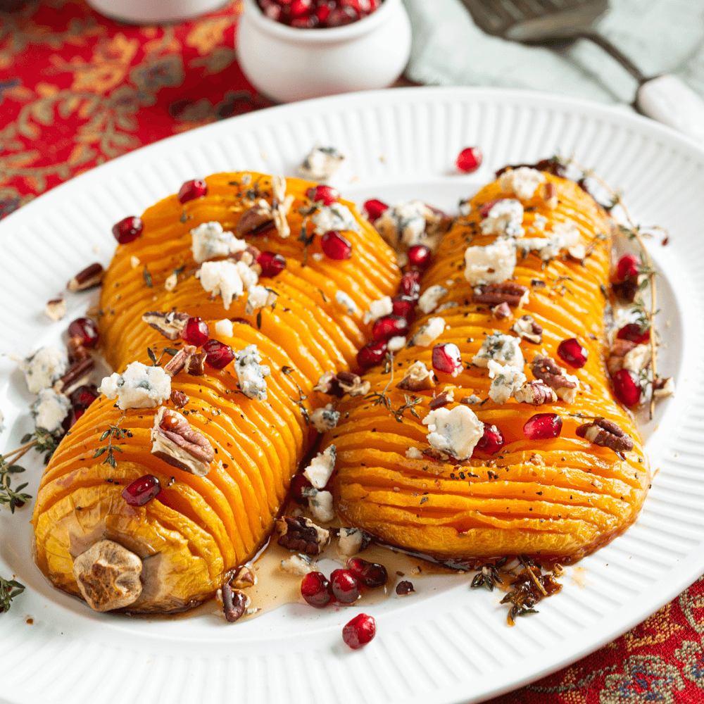 two hassleback-cut roasted butternut squash halves finished with crumbled blue cheese and pomegranate arils