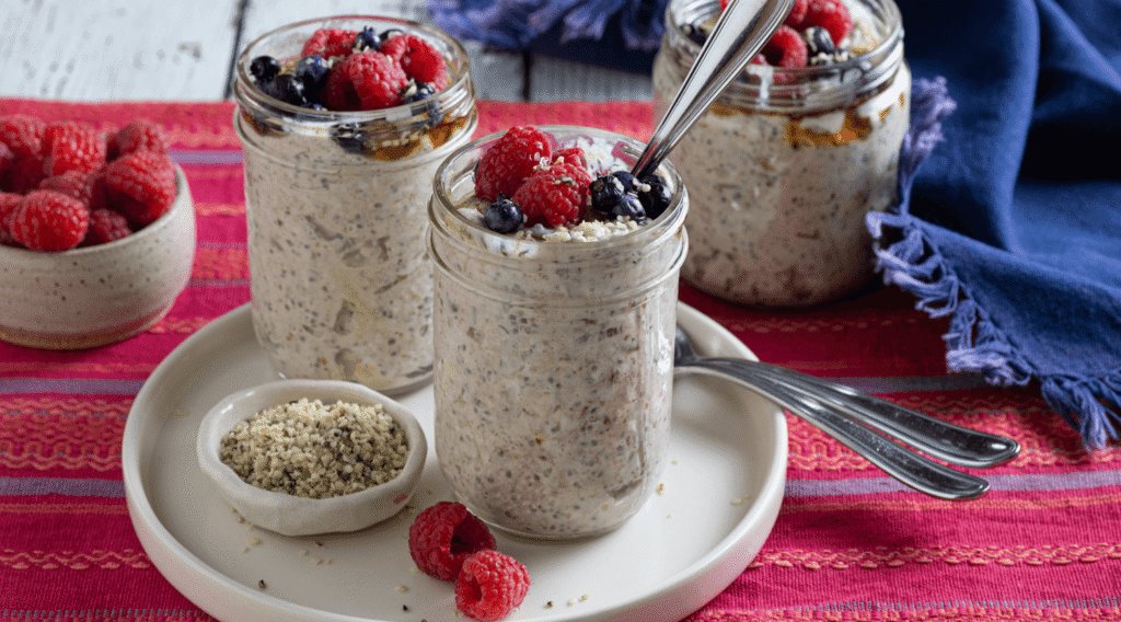 Small white plate with two glass jars of Muesli Overnight Oats garnished with fresh berries