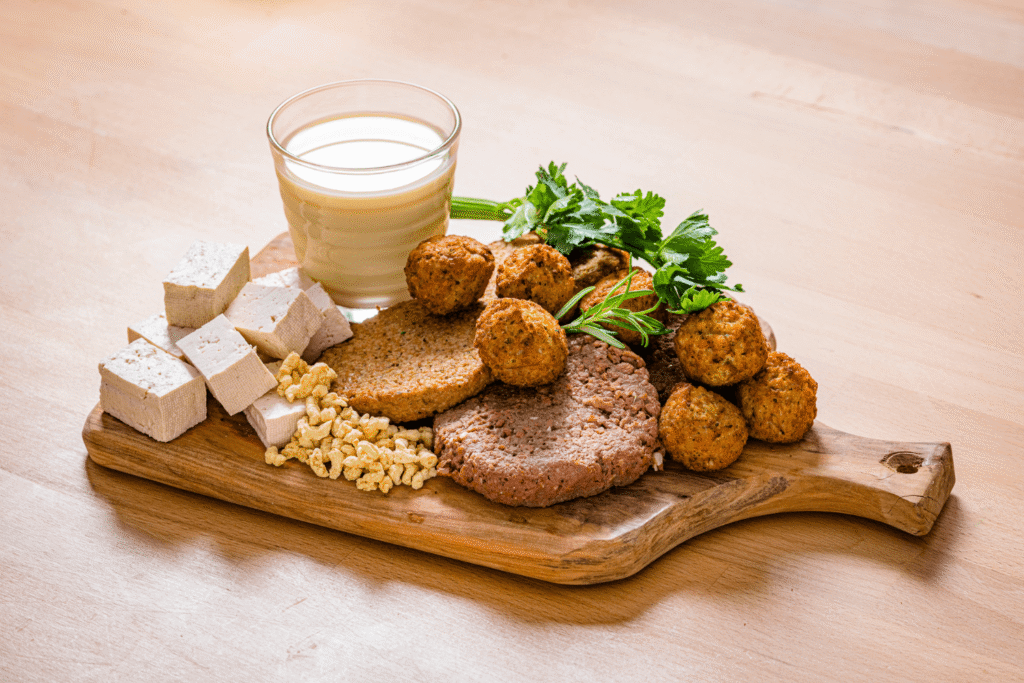 Wooden serving board with assorted sources of plant-based protein like tofu, veggie burger, falafel, and soy milk