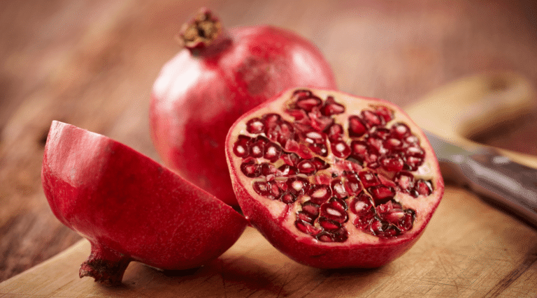 Sliced pomegranate with visible seeds and whole pomegranate on wooden cutting board