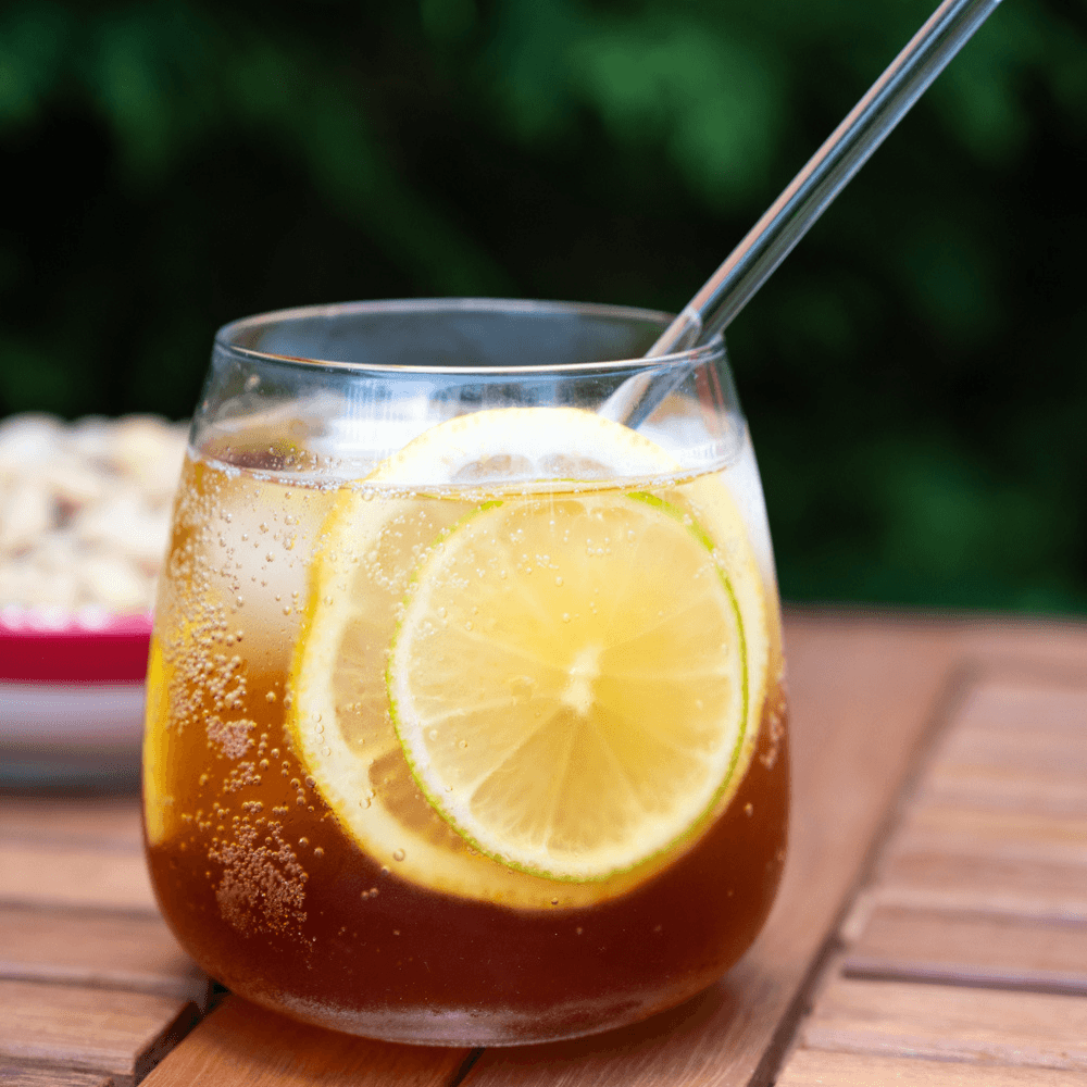 Short tumbler glass of pomegranate fizz with ice cubes and two lemon wheels