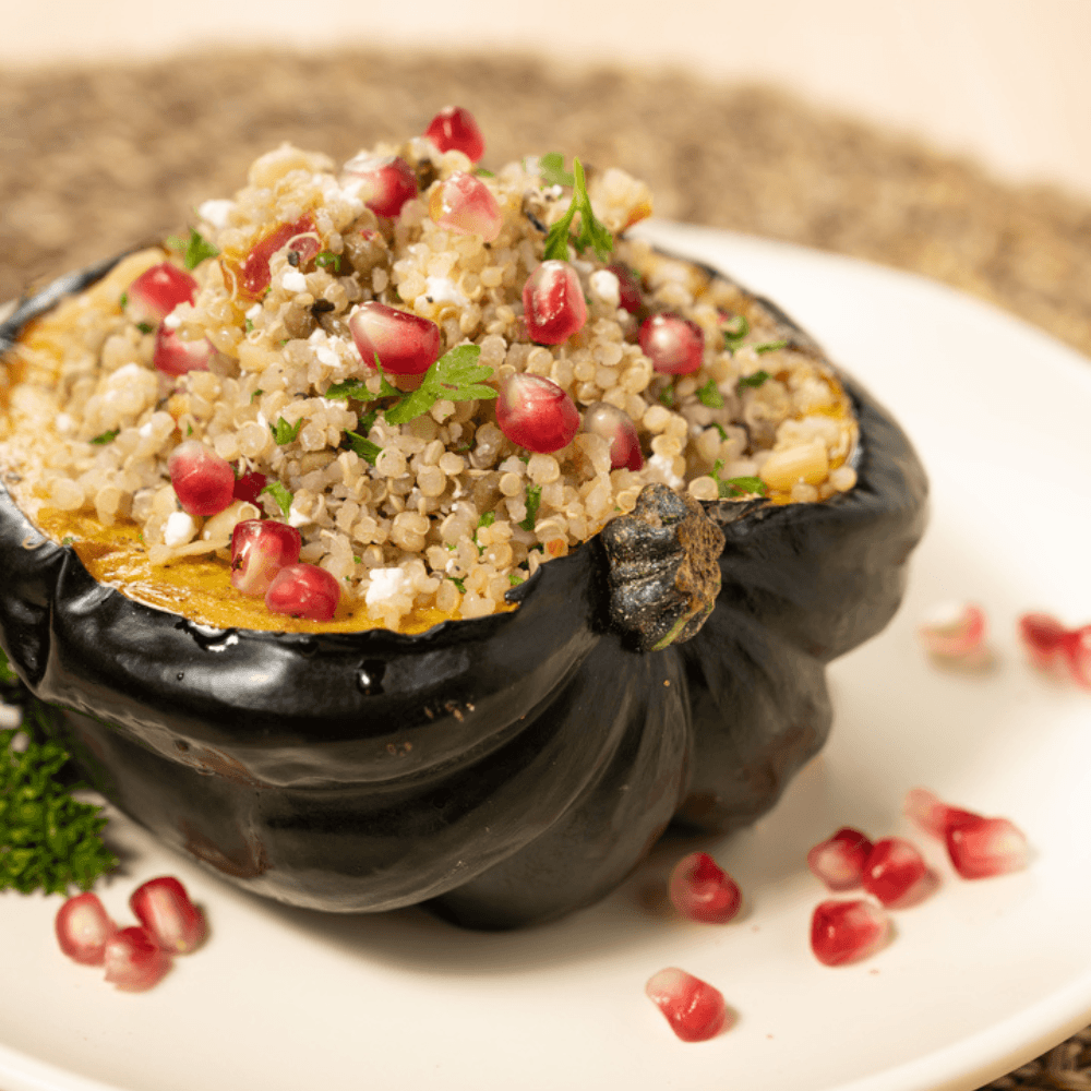 White plate with half an acorn squash stuffed with quinoa and pomegranate arils