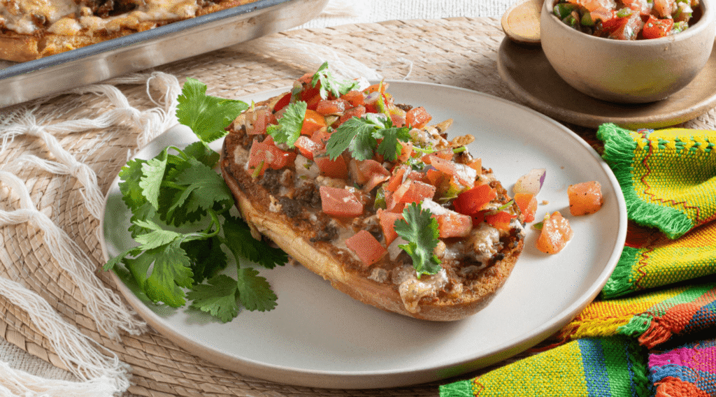White plate with slice of sourdough topped with melted cheese, molletes, and pico de gallo
