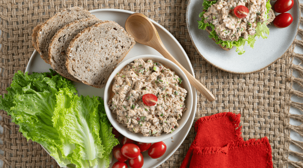 Overhead image of plate with three plain slices of bread and a bowl of spicy tuna salad topped with a halved tomato