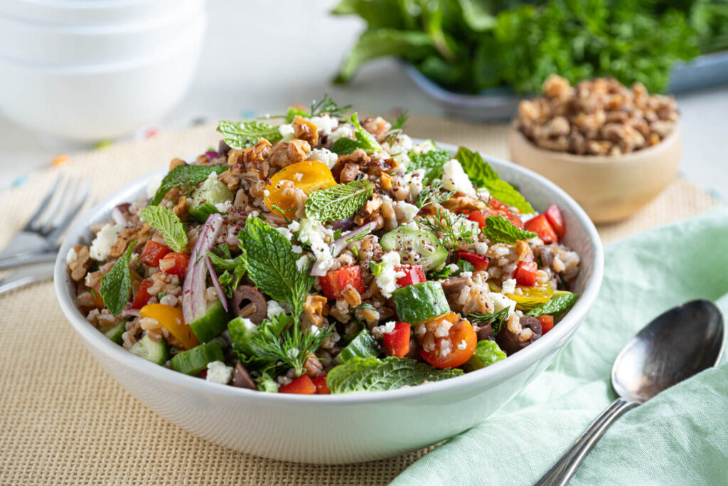 White bowl filled with farro salad recipe and fresh herbs and veggies