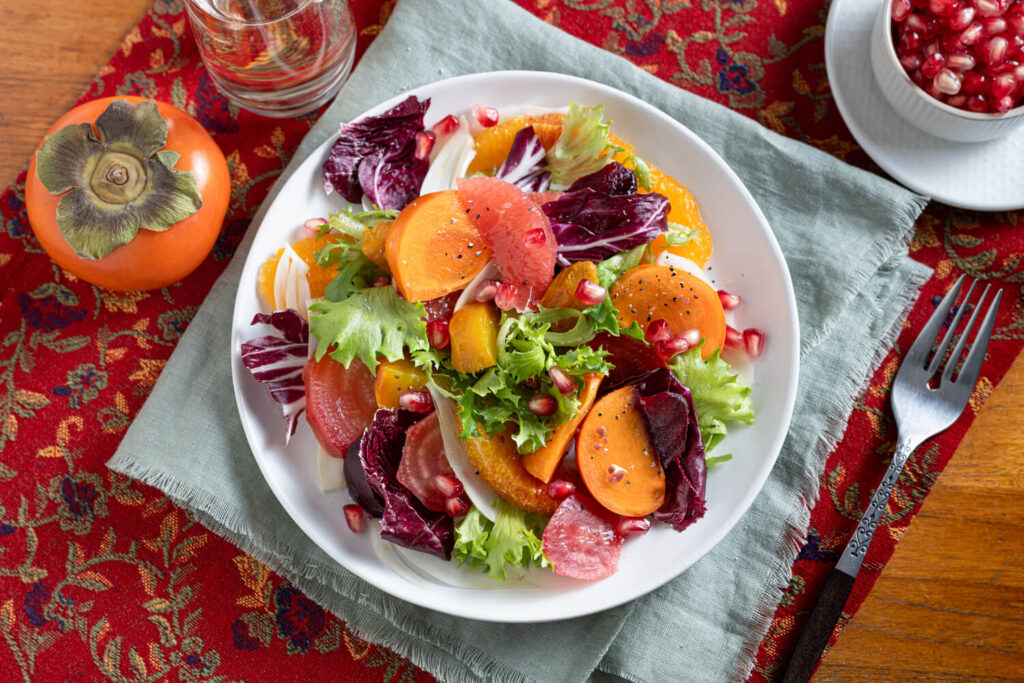 Overhead image of a sald recipe made with mixed greens, radicchio, beets, and persimmons