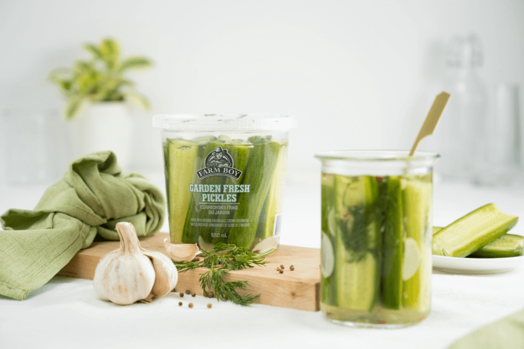 Plastic container of farm Boy Garden Fresh Pickles with glass jar of decanted pickles