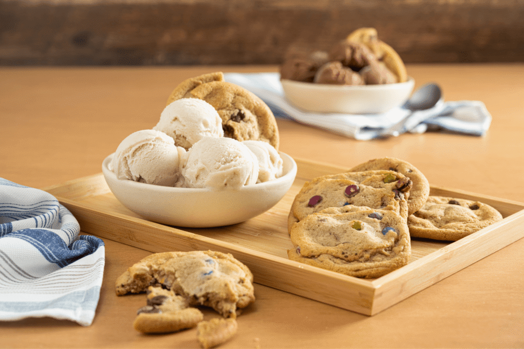 Bowl with scoops of vanilla oat-based ice cream on wooden serving board with plant-based cookies