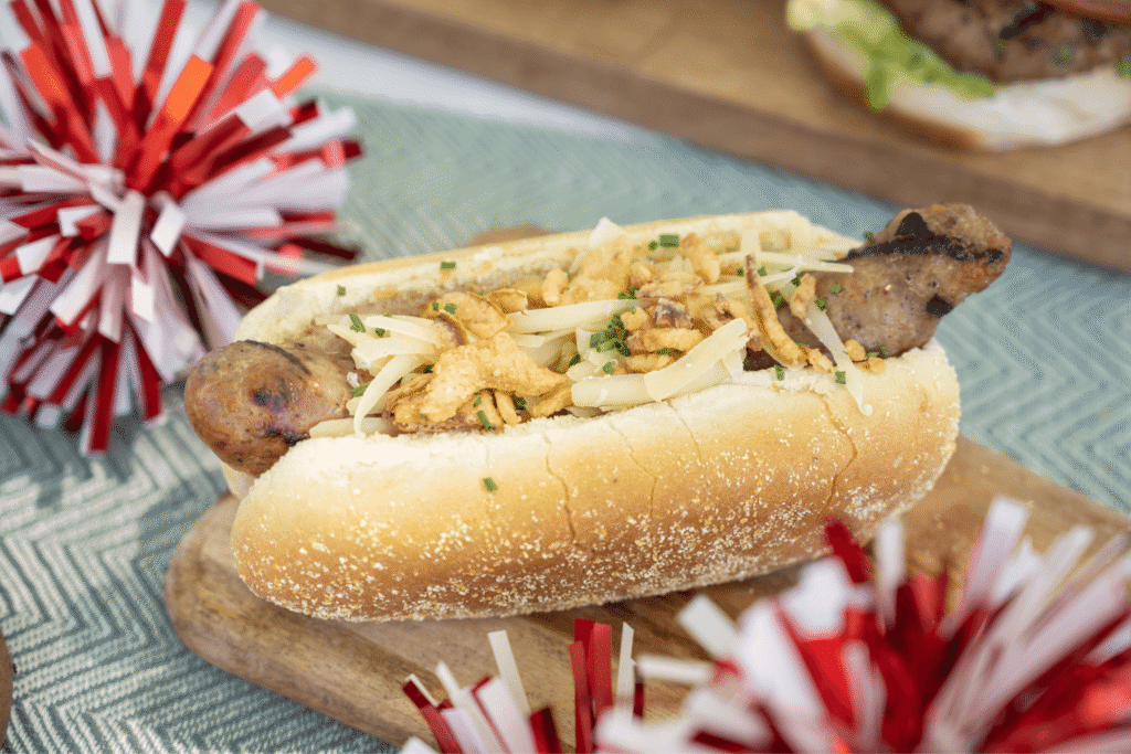 Farm Boy Great Canadian Artisan sausage dressed with cheese and fried onion strings with red and white pom poms for decoration for Canada Day