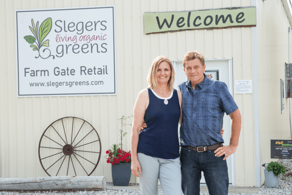 Couple standing in front of building with Slegers Living Organic Greens on sign in front