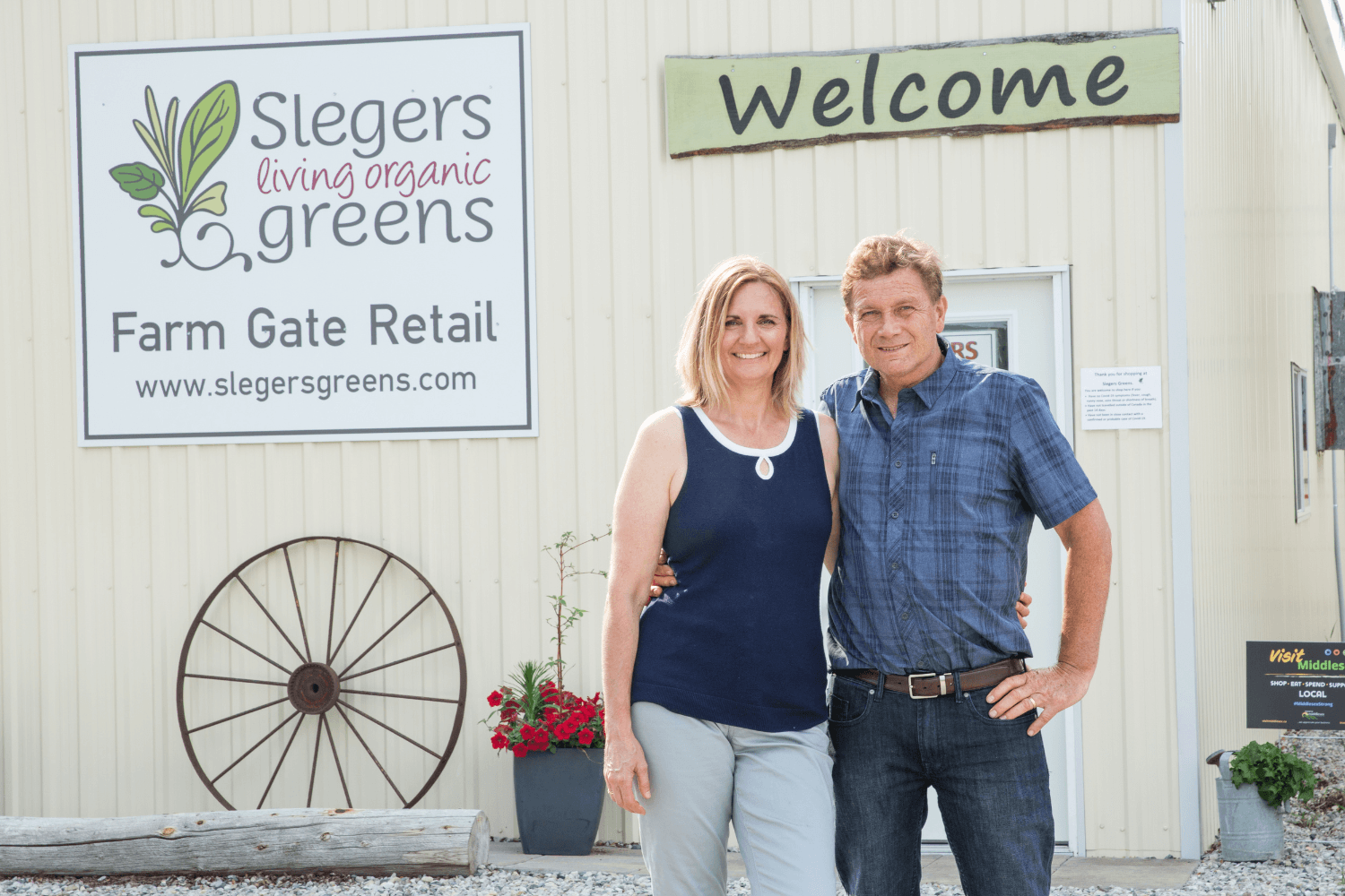 Couple standing in front of building with Slegers Living Organic Greens on sign in front