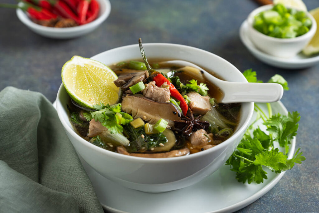 White bowl with chicken soup with asian greens, lime, and chili pepper