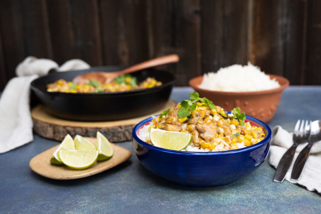Side view of cajun skillet chicken with corn served over rice in a blue bowl