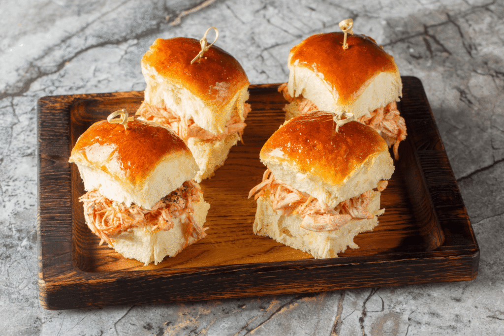 Butter Hawaiian rolls baked with pulled chicken and cheese close-up on a wooden board on the table