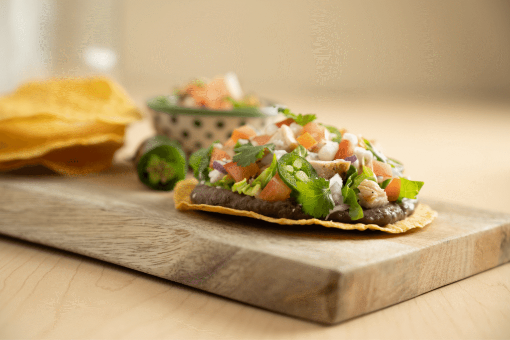 Side image of a corn tostada topped with black beans, chicken, fresh cilantro, and pico de gallo