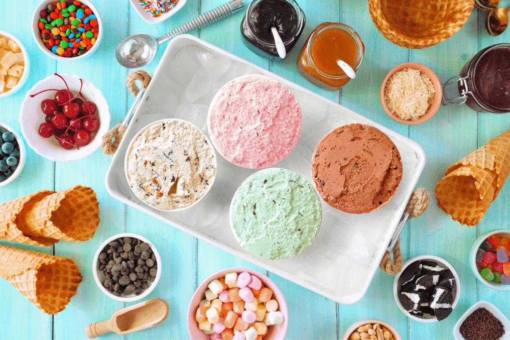 Summer ice cream buffet with different flavors and sweet toppings. Top view table scene on a blue wood background.