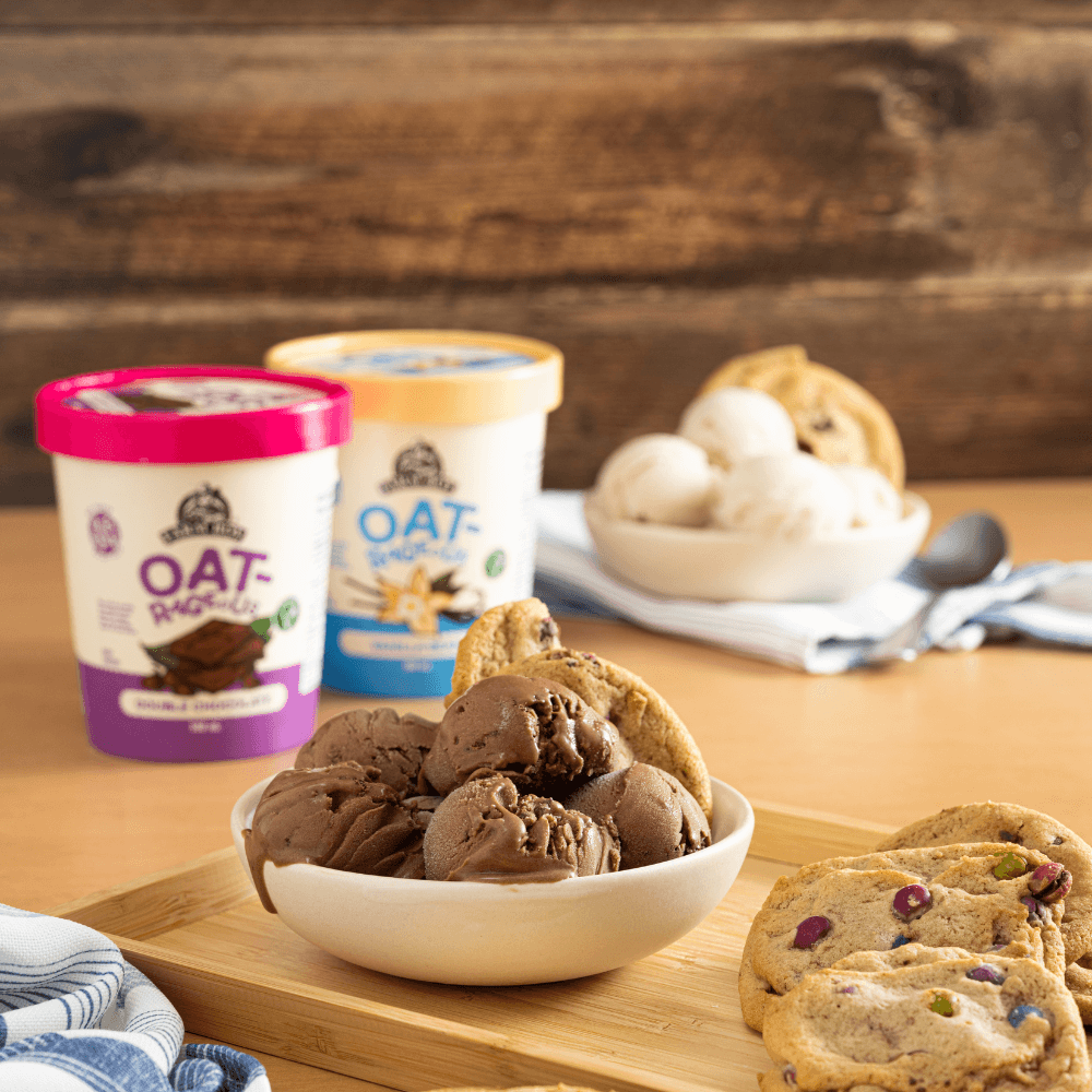 Bowl of chocolate dairy-free ice cream with cookies. Two pint of Farm Boy Oat Rageous Frozen Dessert out of focus in background