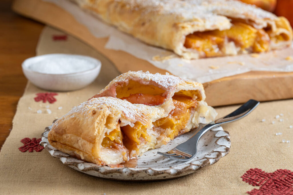 Slice of peach strudel won plate with remaining strudel out of focus in background