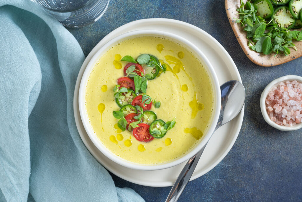Overhead image of white bowl with sweet corn gazpacho garnished with olive oil and fresh jalapeno peppers