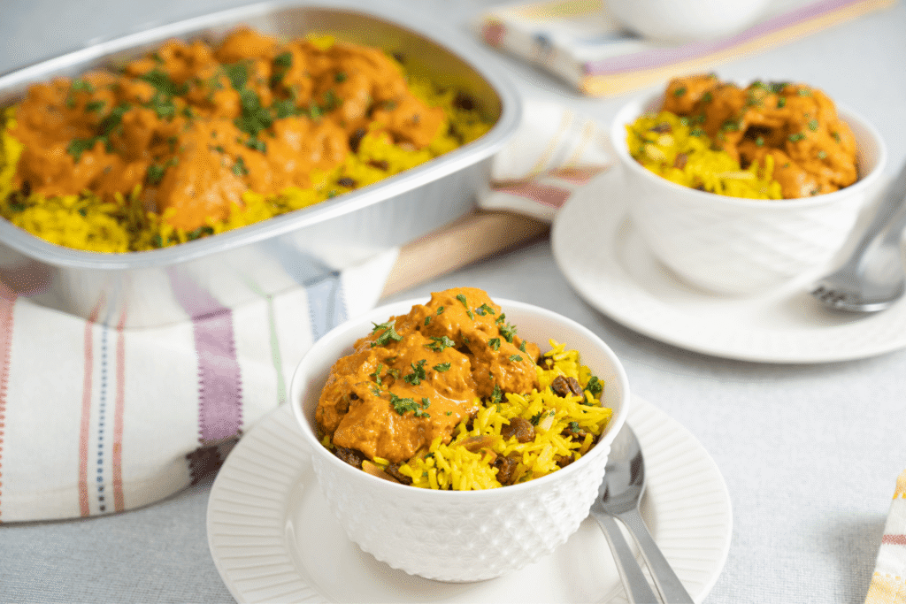 Two bowls of Farm BOy Butter Chicken and Rice with container of Butter Chicken and Rice out of focus in background