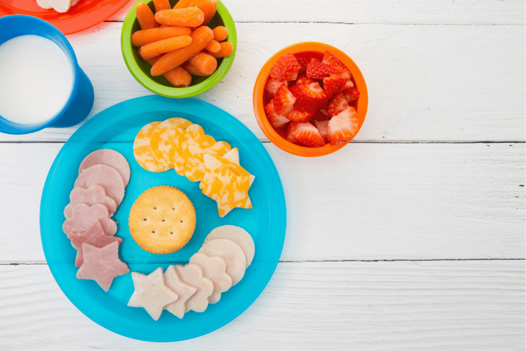 Healthy Lunch for Children on Bright Plates with cheese, crackers, sliced meats, fresh fruits, and vegetables