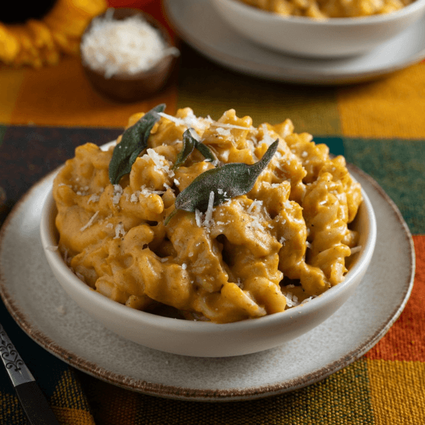 Small white bowl of pumpkin mac and cheese garnished with grated cheese and crispy sage