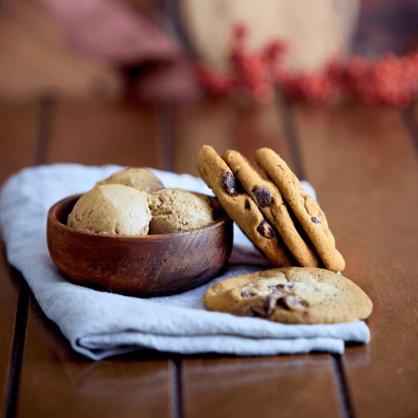 Small wooden bowl with scoops of ice cream beside four chocolate chip cookies